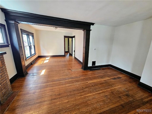 unfurnished room with baseboards, decorative columns, wood finished floors, and visible vents
