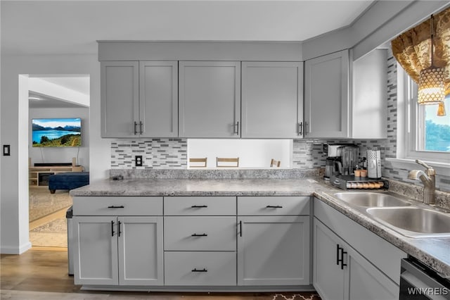 kitchen with backsplash, a sink, dishwashing machine, and light countertops