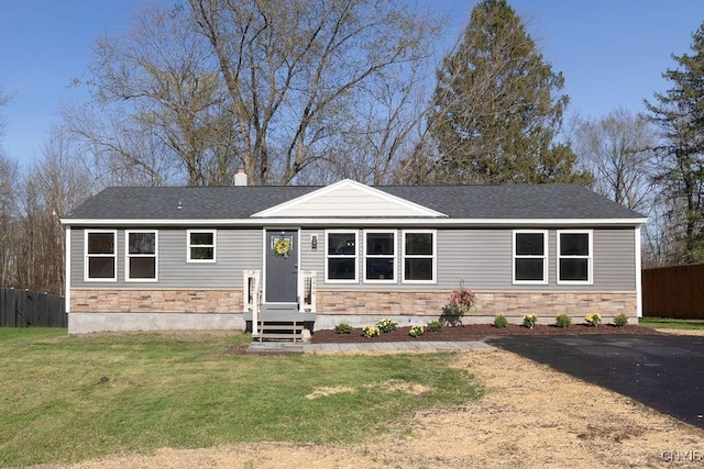 view of front of home featuring roof with shingles, a front yard, fence, and stone siding