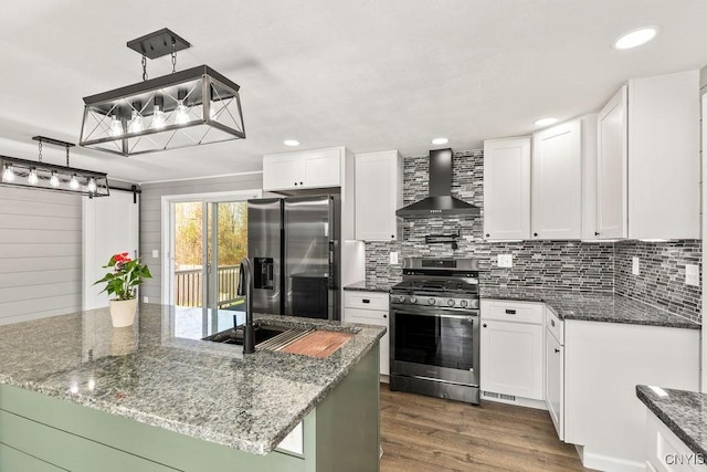 kitchen with wall chimney range hood, white cabinets, appliances with stainless steel finishes, backsplash, and dark wood-style floors