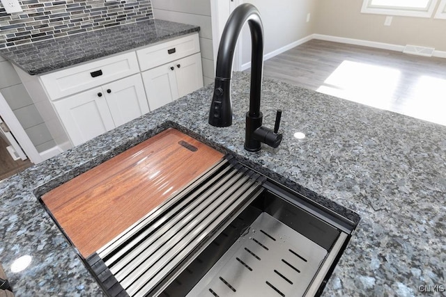 details featuring decorative backsplash, visible vents, wood finished floors, a sink, and baseboards