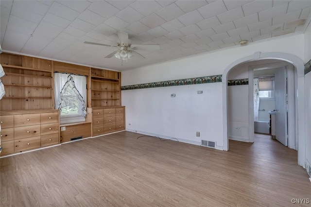 interior space featuring arched walkways, a ceiling fan, baseboards, wood finished floors, and visible vents