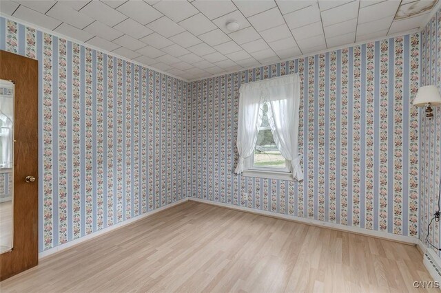 unfurnished room featuring baseboards, wallpapered walls, and wood finished floors