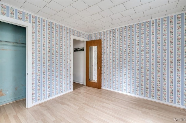 unfurnished bedroom featuring baseboards, wallpapered walls, wood finished floors, and a closet