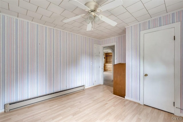 interior space with ceiling fan, arched walkways, baseboard heating, wood finished floors, and wallpapered walls