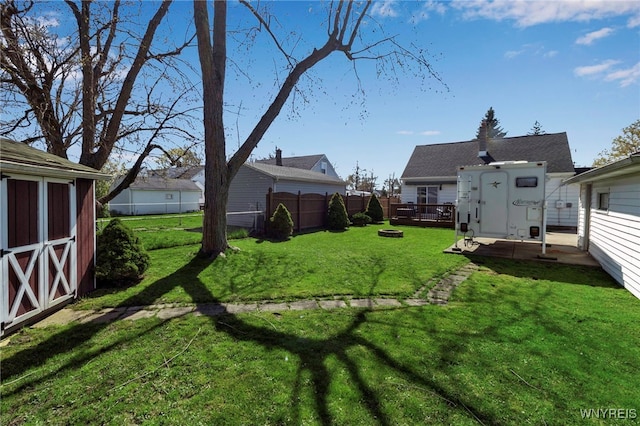 view of yard with a storage unit, fence, an outbuilding, and a deck