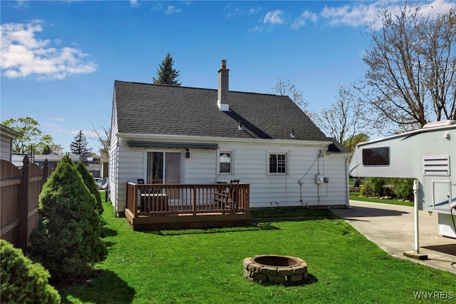 rear view of house with fence, a wooden deck, a chimney, a lawn, and a fire pit
