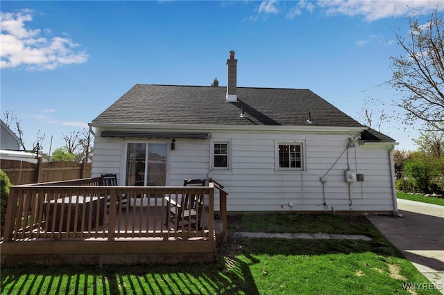 back of property with a chimney, roof with shingles, a lawn, a deck, and fence