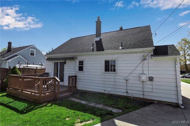 back of property featuring fence, a deck, roof with shingles, a chimney, and a lawn