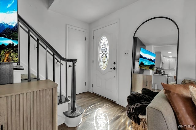 foyer entrance with stairs, arched walkways, and wood finished floors
