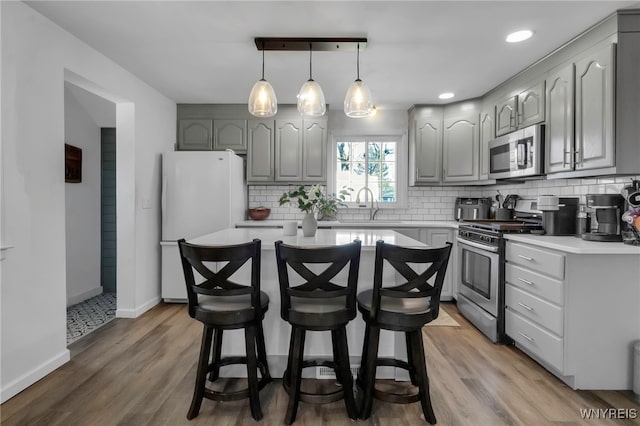 kitchen with light countertops, gray cabinets, appliances with stainless steel finishes, and a breakfast bar area