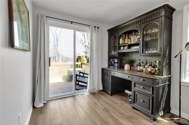 bar with baseboards, a bar, light wood-type flooring, and visible vents