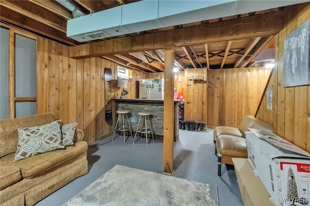 finished below grade area with a dry bar, freestanding refrigerator, wood walls, and visible vents