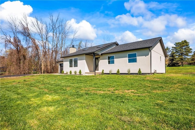 ranch-style home with a garage, a chimney, a front yard, and stucco siding