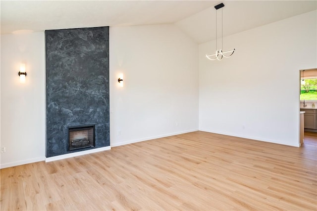 unfurnished living room with light wood-style floors, a notable chandelier, vaulted ceiling, and a premium fireplace