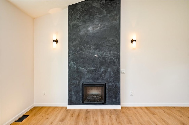 unfurnished living room with visible vents, baseboards, wood finished floors, and a large fireplace