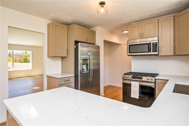 kitchen featuring a peninsula, light stone countertops, light wood-style floors, baseboards, and appliances with stainless steel finishes