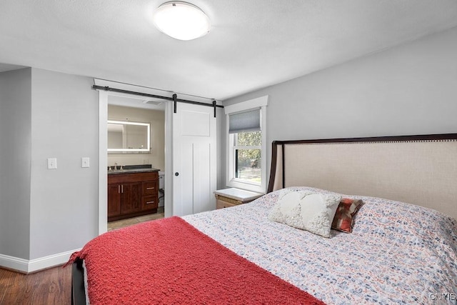 bedroom with baseboards, ensuite bathroom, a barn door, and wood finished floors