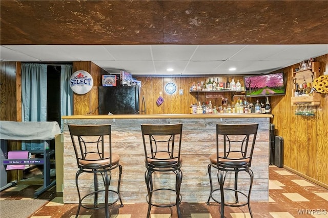 bar featuring freestanding refrigerator, wood walls, a paneled ceiling, tile patterned floors, and a dry bar