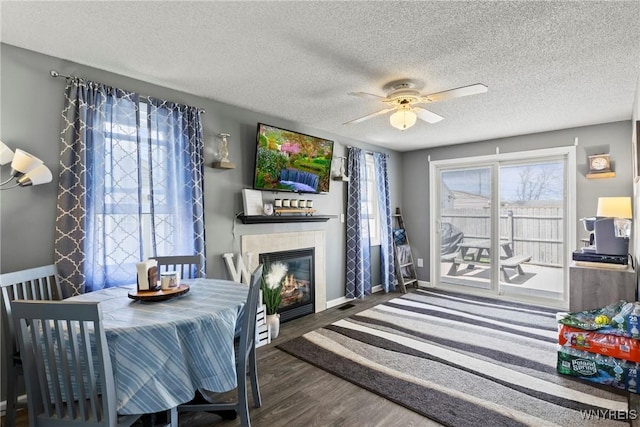 interior space with a ceiling fan, a textured ceiling, a tiled fireplace, wood finished floors, and baseboards