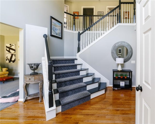 stairway featuring baseboards, a towering ceiling, and wood finished floors