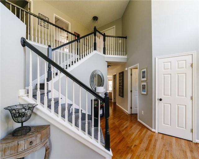 staircase with baseboards, a towering ceiling, and wood finished floors