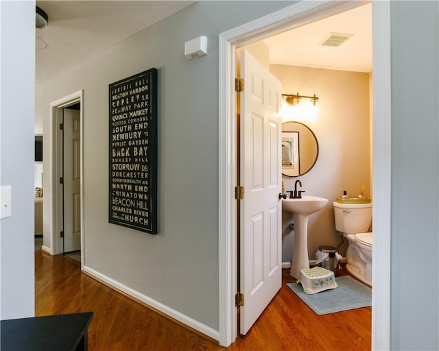 hall with a sink, baseboards, visible vents, and wood finished floors