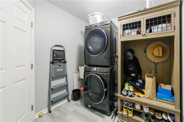 clothes washing area with a textured ceiling, laundry area, stacked washing maching and dryer, and baseboards