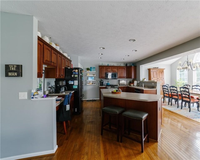 kitchen featuring a kitchen island, a textured ceiling, appliances with stainless steel finishes, light countertops, and dark wood-style floors