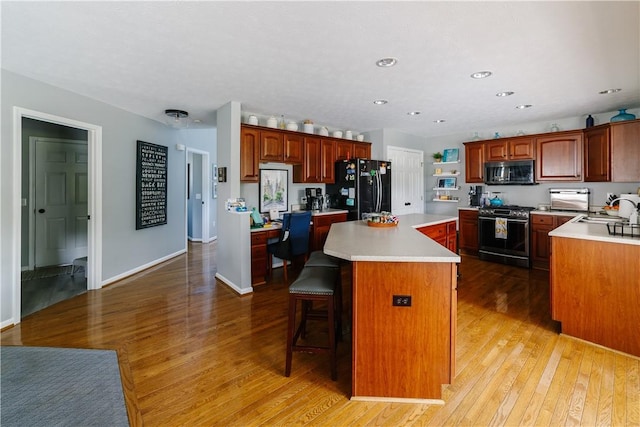kitchen featuring freestanding refrigerator, a kitchen island, stainless steel range with gas cooktop, light wood-type flooring, and light countertops
