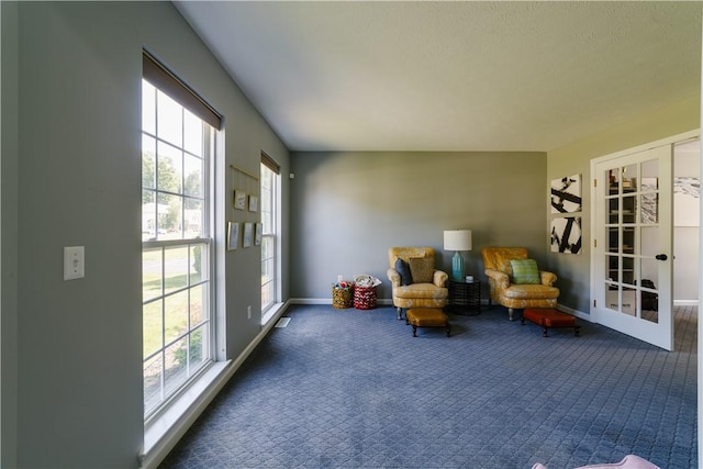 sitting room with baseboards, plenty of natural light, and dark colored carpet