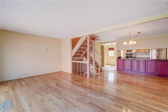 unfurnished living room with stairway, an inviting chandelier, light wood-style floors, and visible vents