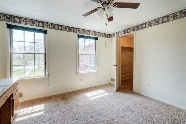 unfurnished bedroom with baseboards, a walk in closet, light carpet, and ceiling fan