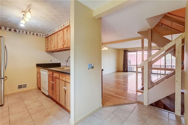 kitchen with visible vents, white dishwasher, dark countertops, a sink, and light tile patterned flooring