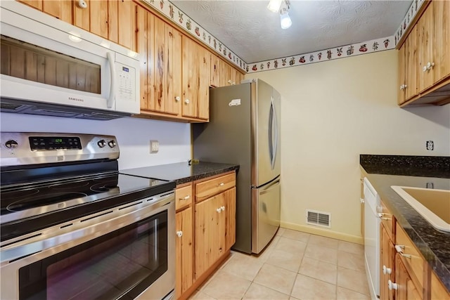kitchen featuring light tile patterned flooring, a sink, stainless steel appliances, baseboards, and visible vents