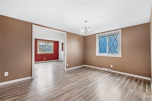 unfurnished dining area featuring baseboards, an inviting chandelier, wood finished floors, and visible vents