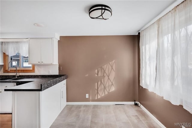 kitchen featuring a sink, dark countertops, baseboards, and white cabinets