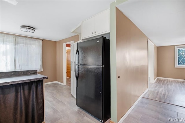 kitchen featuring light tile patterned floors, baseboards, freestanding refrigerator, and white cabinetry