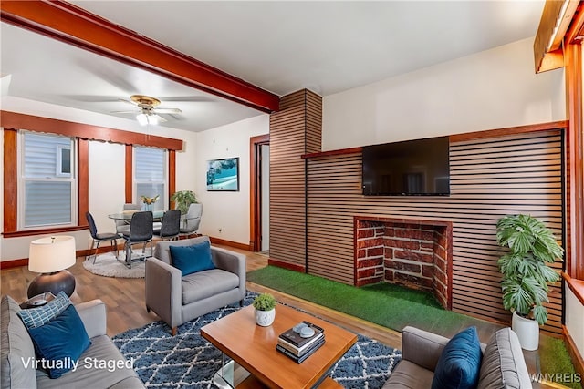 living area featuring baseboards, beamed ceiling, a ceiling fan, and wood finished floors