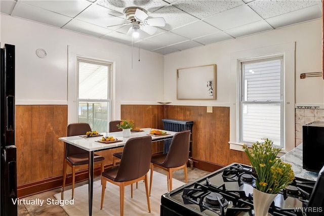 dining area featuring a ceiling fan, a paneled ceiling, a wainscoted wall, and wooden walls