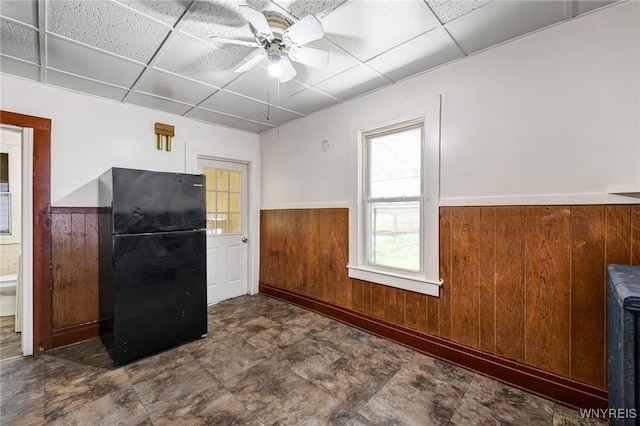 kitchen with wooden walls, ceiling fan, a paneled ceiling, a wainscoted wall, and freestanding refrigerator