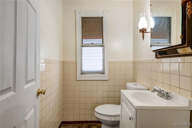 half bath featuring tile walls, a wainscoted wall, vanity, and toilet