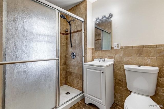 bathroom with vanity, toilet, a wainscoted wall, tile walls, and a stall shower