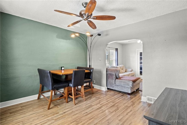 dining area with a ceiling fan, a textured ceiling, visible vents, arched walkways, and wood finished floors