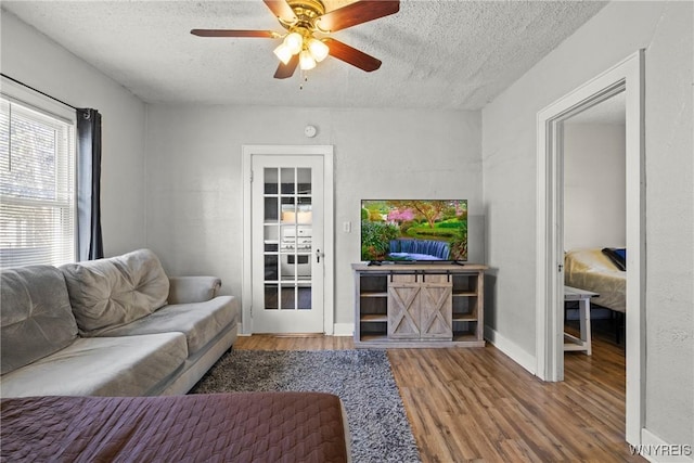 living area featuring baseboards, a ceiling fan, a textured ceiling, and wood finished floors