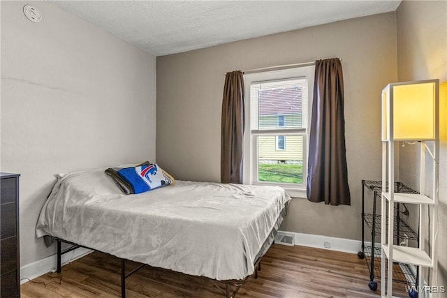 bedroom featuring a textured ceiling, baseboards, visible vents, and wood finished floors
