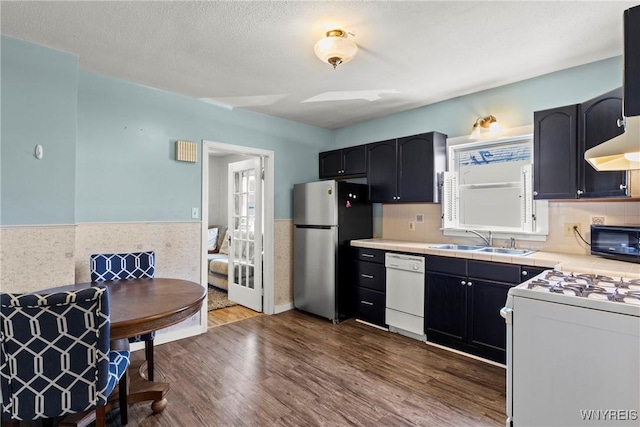 kitchen featuring dark wood-style flooring, white appliances, light countertops, a wainscoted wall, and a sink
