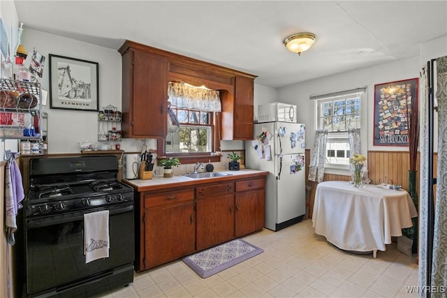 kitchen featuring freestanding refrigerator, light countertops, brown cabinets, a sink, and gas stove