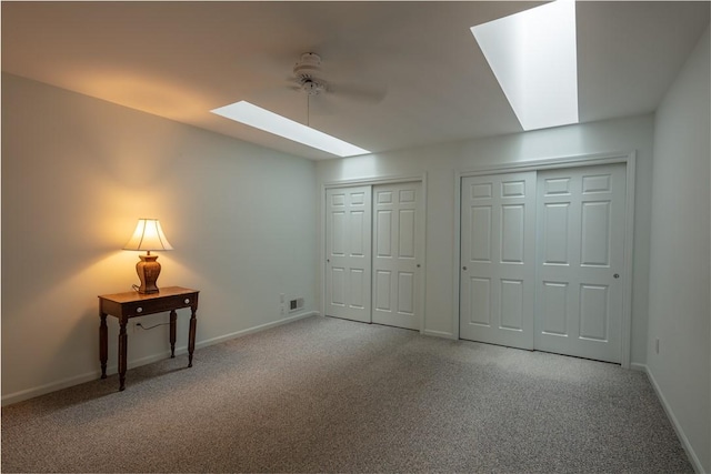 unfurnished bedroom with visible vents, a skylight, baseboards, two closets, and carpet flooring