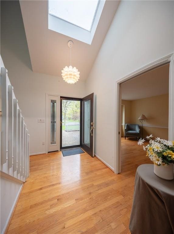 entrance foyer with light wood-style floors, high vaulted ceiling, a chandelier, baseboards, and a skylight